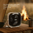Rechargeable mini fan with LED emergency light and USB on a wooden table with a campfire in the background.