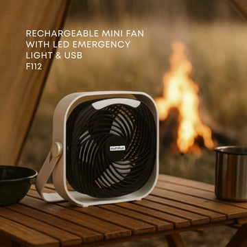 Rechargeable mini fan with LED emergency light and USB on a wooden table with a campfire in the background.