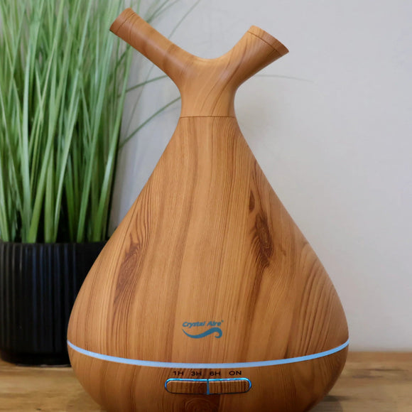 Wooden diffuser on a wooden surface with a plant in the background